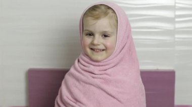Islak saçlı küçük kız pembe havlunun içinde saklanıyor. Banyo yaptıktan sonra gülümser.