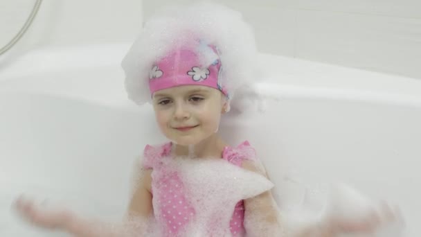 Милая блондинка принимает ванну в купальнике. Маленький ребенок моет голову — стоковое видео