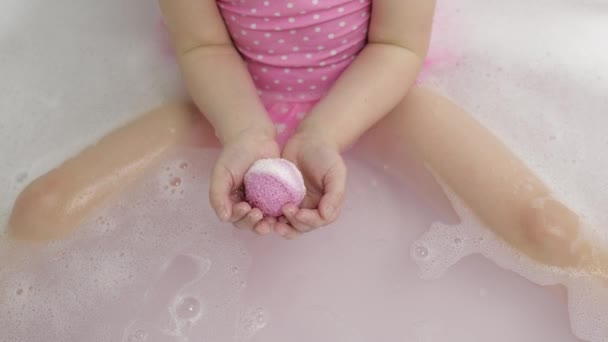 Flickans händer sätter badbomben i vatten. Ball av badsalt löses upp i vatten — Stockvideo