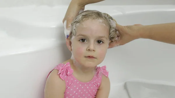 Χαριτωμένο ξανθό κορίτσι κάνει μπάνιο με μαγιό. Μικρό παιδί πλένει το κεφάλι της — Φωτογραφία Αρχείου