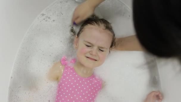 Nettes blondes Mädchen nimmt ein Bad in Badebekleidung. Kleines Kind wäscht sich den Kopf — Stockvideo