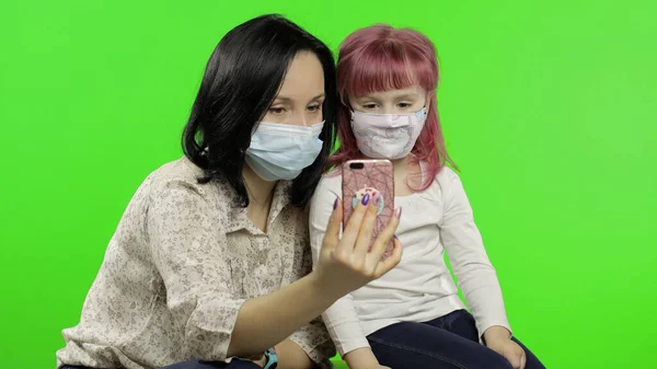 Mother, daughter wearing medical mask holding smart phone talking on video call