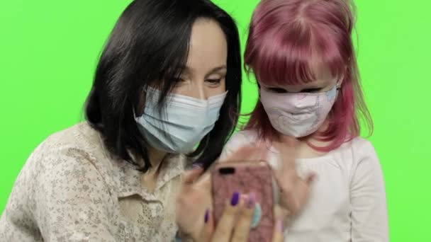 Anne ve kızı tıbbi maske takıyor. Elinde akıllı bir telefonla konuşuyor. — Stok video