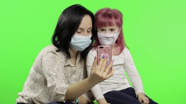 Мама, дочь в медицинской маске, держат смартфон, разговаривают на видео. — стоковое видео