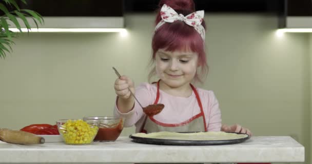 Matlagning pizza. Liten barn i förkläde lägga tomatsås till deg i köket — Stockvideo