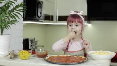 Pizza pişiriyorum. Önlüklü küçük çocuk mutfakta hamura rendelenmiş peynir ekliyor.