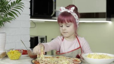 Pizza pişiriyorum. Önlüklü küçük çocuk mutfakta hamura rendelenmiş peynir ekliyor.