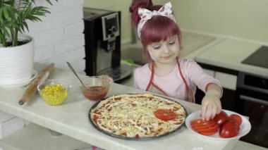 Pizza pişiriyorum. Önlüklü küçük çocuk mutfakta hamura doğranmış domates ekliyor.