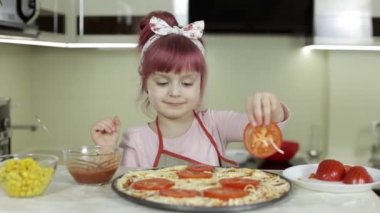 Pizza pişiriyorum. Önlüklü küçük çocuk mutfakta hamura doğranmış domates ekliyor.