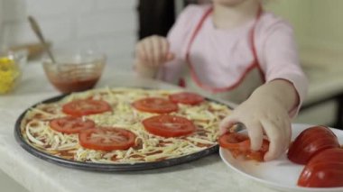 Pizza pişiriyorum. Önlüklü küçük çocuk mutfakta hamura doğranmış domates ekliyor.