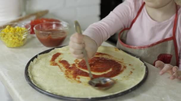 Pizza kochen. Kleines Kind in Schürze fügt Tomatensauce zum Teig in der Küche hinzu — Stockvideo