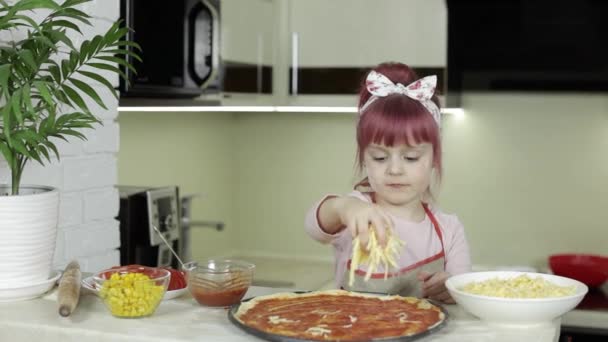 Cucinare la pizza. Bambino in grembiule che aggiunge formaggio grattugiato alla pasta in cucina — Video Stock