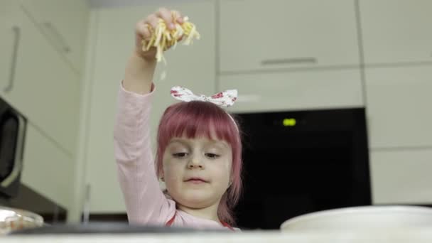 Готовлю пиццу. Маленький ребенок в фартуке добавляет тертый сыр в тесто на кухне — стоковое видео