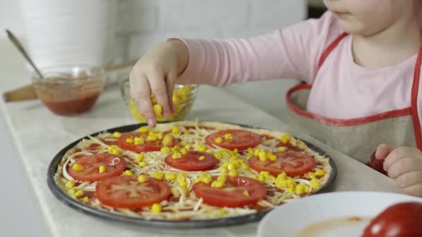 ピザを作る。台所の生地に缶詰のトウモロコシを追加エプロンの小さな子供 — ストック動画