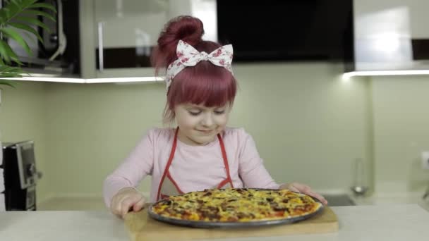 Pizzát főzök. Kötényes kisgyerek frissen sült forró pizzával a konyhában. — Stock videók