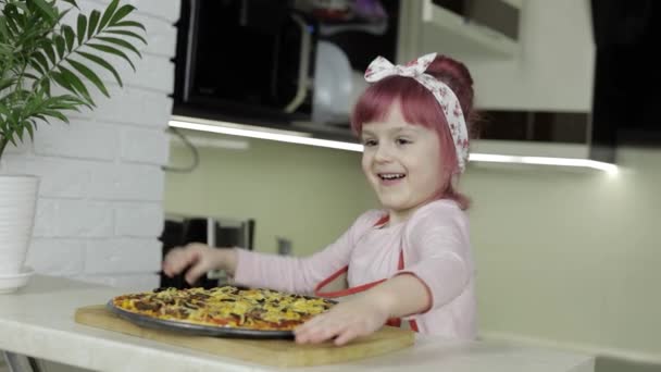 Pizzát főzök. Kötényes kisgyerek frissen sült forró pizzával a konyhában. — Stock videók