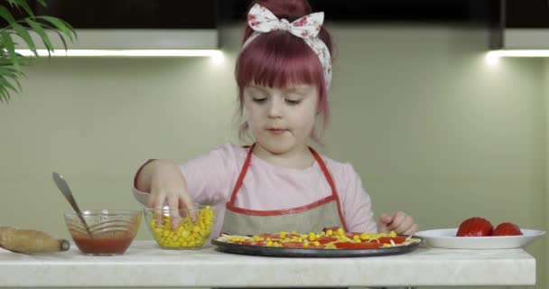 Cocinar pizza. Niño pequeño en delantal añadiendo maíz enlatado a la masa en la cocina — Vídeos de Stock