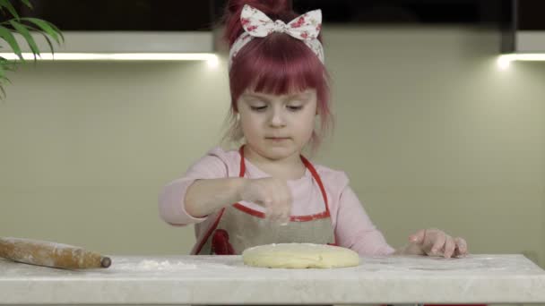 Готовлю пиццу. Маленький ребенок в фартуке посыпать тесто мукой на кухне — стоковое видео