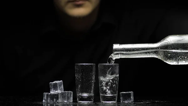 Il barman versa la vodka congelata da bottiglia in due occhiali con ghiaccio. Fondo nero Immagini Stock Royalty Free