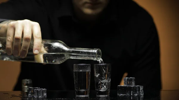 Il barman versa la vodka congelata da bottiglia in due occhiali con ghiaccio. Sfondo marrone Foto Stock Royalty Free