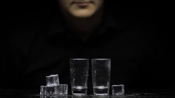 Ο μπάρμαν ρίχνει παγωμένη βότκα από το μπουκάλι σε δύο ποτήρια με πάγο. Μαύρο φόντο — Αρχείο Βίντεο