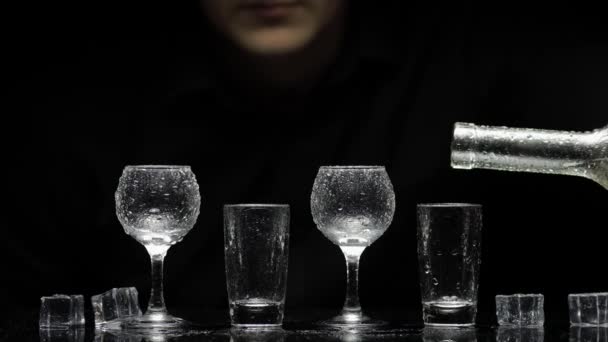 Barman wlewa zamrożoną wódkę z butelki do szklanek z lodem. Czarne tło — Wideo stockowe