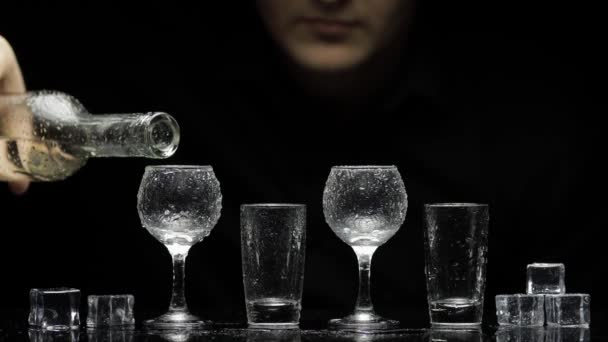 Bartender hälla fryst vodka från flaska i glas med is. Svart bakgrund — Stockvideo