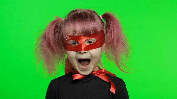 Funny niña en traje y máscara juega super héroe. Día nacional del superhéroe —  Fotos de Stock