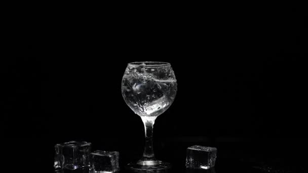 Добавить кубик льда, чтобы выстрел водки в стекло на черном фоне. Алкогольный напиток — стоковое видео
