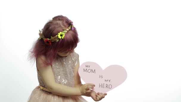 Девочка принцесса держит розовое бумажное сердце с текстом о матери. День матери — стоковое видео