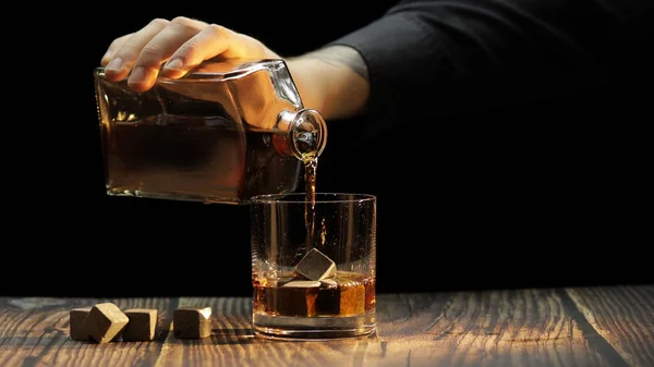 Pouring whiskey, cognac into glass. Black background. Pour of alcohol drink — Stock Photo, Image