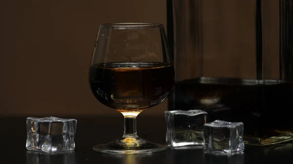 Алкоголь пьет виски, коньяк в стакане со льдом. Половина бутылки на столе — стоковое фото