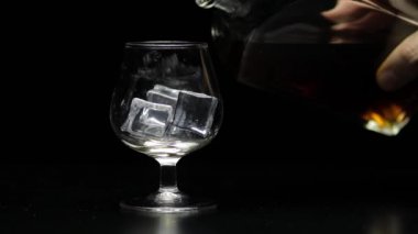 Viski ve konyağı cama döküyorum. Siyah arka plan. Alkol içeceği.