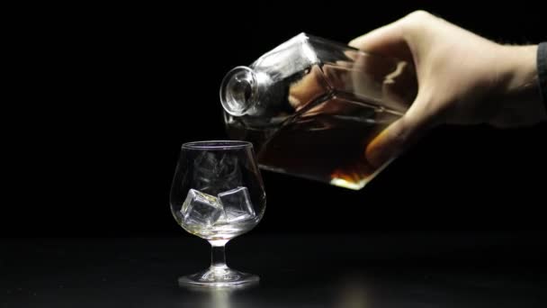 ウィスキーを入れてコニャックをグラスに。黒の背景。酒を注ぐ — ストック動画
