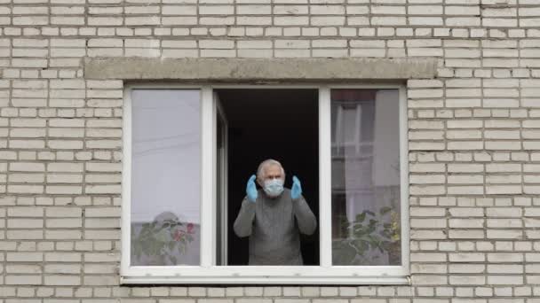 El viejo abuelo se queda en la ventana aislado en casa en cuarentena. Coronavirus — Vídeos de Stock