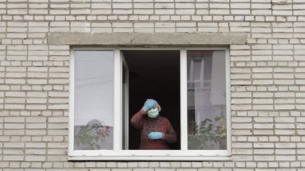 La abuela anciana se queda en la ventana aislada en casa en cuarentena. Coronavirus — Vídeos de Stock