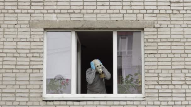 Ein alter Mann mit Gasmaske steht isoliert zu Hause am Fenster und steht unter Quarantäne. Coronavirus
