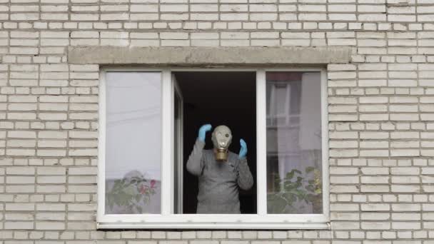 Velho de máscara de gás dança na janela isolado em casa em quarentena. Coronavírus — Vídeo de Stock