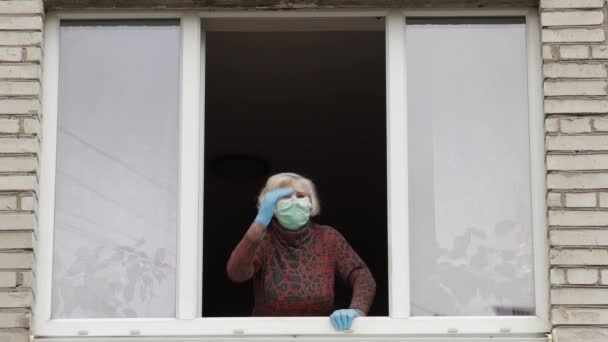 Старуха-бабушка сидит дома в изоляции у окна на карантине. Коронавирус — стоковое видео