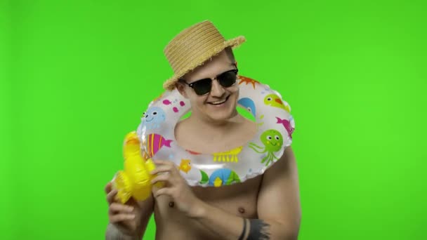 Mladý muž bez košile turista s plaveckým prstenem na ramenou hraje s kachní hračkou — Stock video