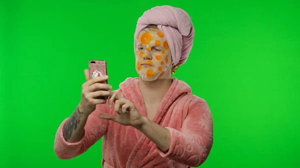 Uomo transessuale in accappatoio con maschera facciale utilizzando il telefono cellulare per videochiamate — Foto Stock