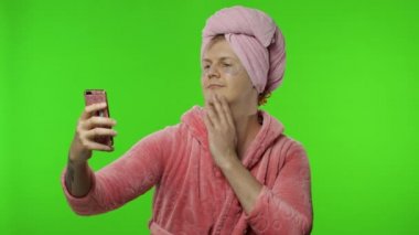 Bornozlu transseksüel adamın portresi cep telefonuyla selfie çekiyor.