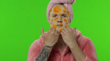 Bornozlu transseksüel bir adamın portresi aynada yüz maskesi takıyor.
