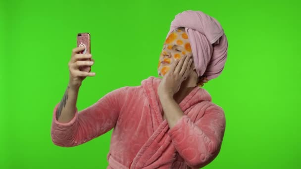 Транссексуальний чоловік в халаті з маскою для обличчя робить селфі за допомогою мобільного телефону — стокове відео