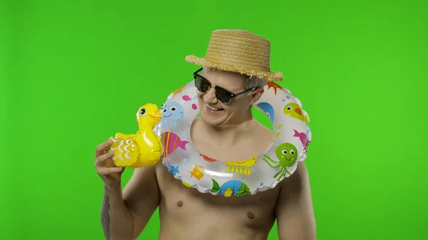 Shirtless young man tourist with swimming ring on shoulders plays with duck toy — Stock Photo, Image