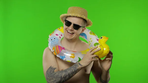 Shirtless young man tourist with swimming ring on shoulders plays with duck toy — Stock Photo, Image