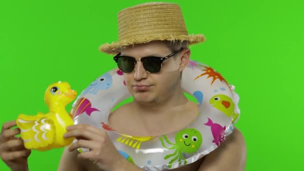 Без сорочки молодий чоловік турист з плавальним кільцем на плечах грає з качиною іграшкою — стокове відео