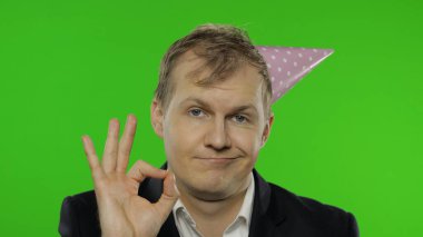 Şenlik şapkasıyla akşamdan kalma sarhoş genç iş adamı, tamam işareti gösteriyor.