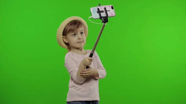 Girl child makes selfie, blogging on mobile phone using selfie stick. Chroma key