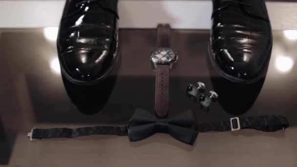 Wedding grooms bow tie, cufflinks, clock and shoes lie on glass table — Stock Video